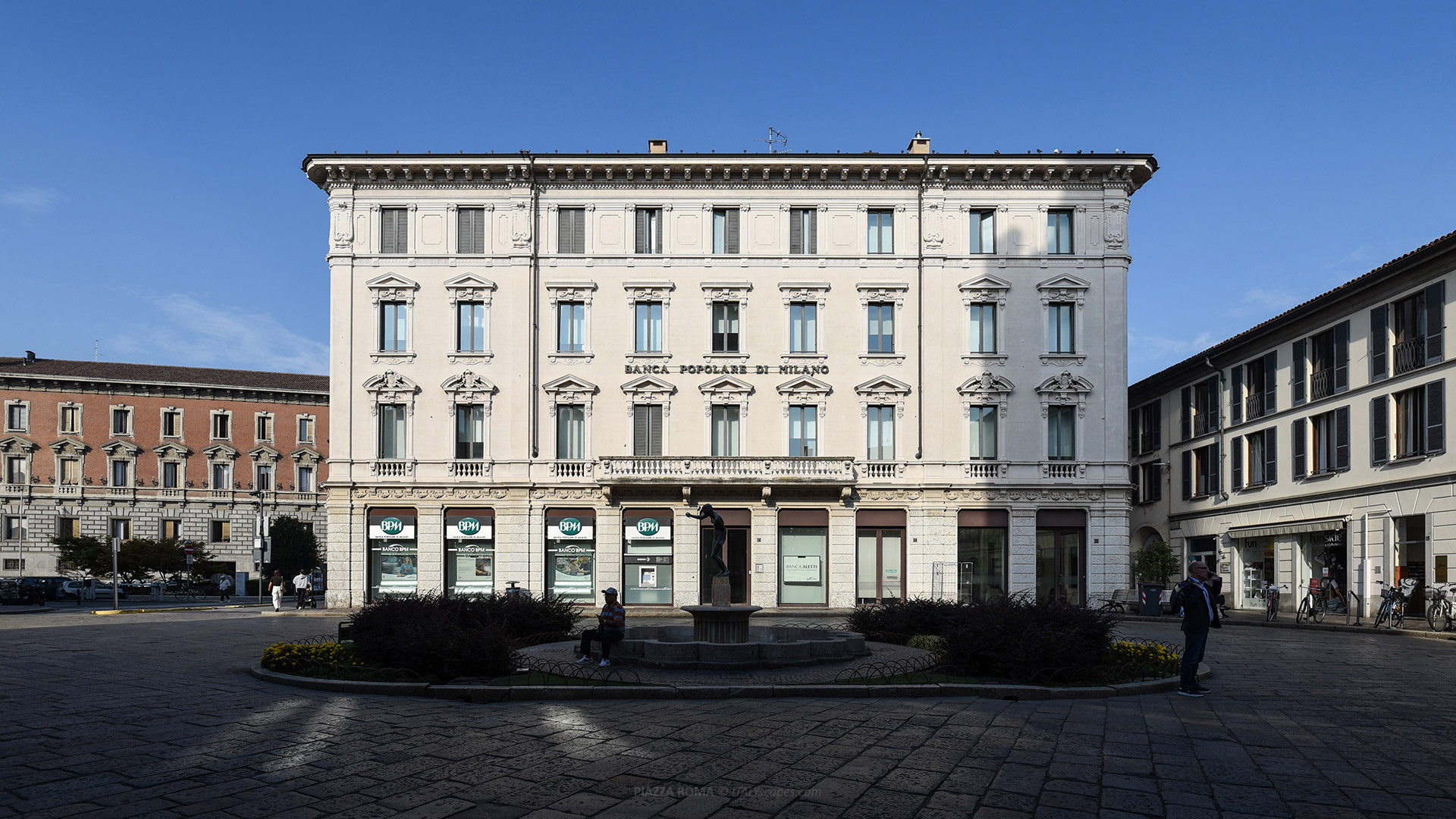 Piazza Roma in Monza with the Fontana delle Rane and Palazzo Piazza Roma 10 under a clear blue sky